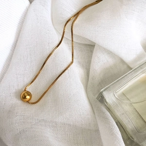 Minimalist gold ball pendant necklace with elegant box chain on soft white linen background