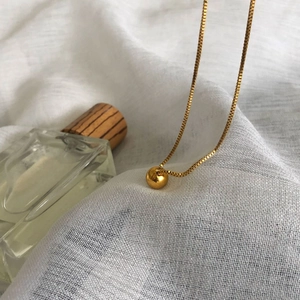 Minimalist gold round ball pendant necklace with box chain on elegant white fabric