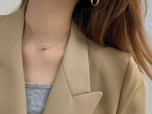 Detail of minimalist gold sphere pendant necklace and matching hoop earrings on model
