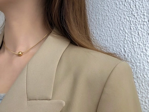 Detail of a minimalist gold ball pendant necklace worn on neck with a beige blazer