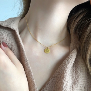 Dettaglio di una collana con moneta occhio greco dorata indossata da una modella