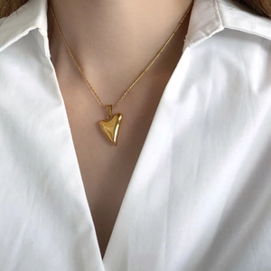 Close-up of a 3D polished gold heart pendant necklace worn on a white shirt
