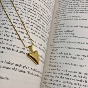 Close-up of a polished gold heart pendant necklace placed on an open book background