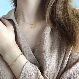 Dettaglio di una collana con moneta occhio greco dorata e bracciale a corda su modella