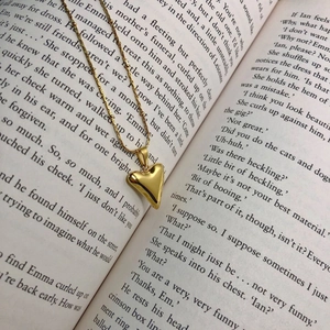 Polished gold 3D heart pendant necklace on an open vintage book page background
