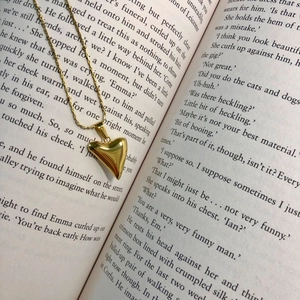 Detailed view of a 3D polished gold heart pendant resting on an open vintage book page