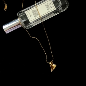 Detail of a 3D gold heart pendant necklace draped elegantly over a luxury perfume bottle