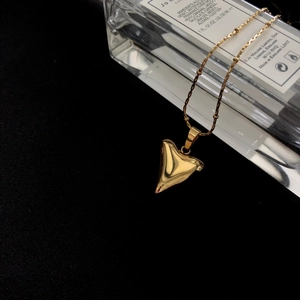 Polished gold shark tooth pendant necklace with bead chain on a dark textured background