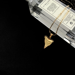 Polished gold shark tooth pendant necklace draped over a perfume bottle
