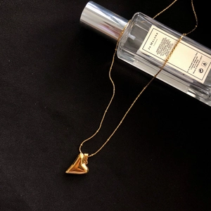 Golden necklace with polished 3D heart pendant on black fabric with perfume bottle