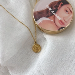 Elegant gold coin necklace with floral relief and geometric pendant on soft fabric background