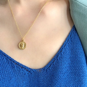 Portrait relief coin pendant necklace in gold finish worn on a dark knit sweater