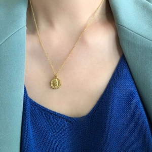 Close-up of gold coin pendant necklace featuring a religious portrait relief on a thin chain