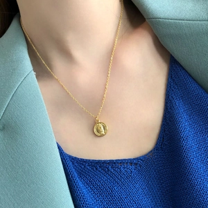 Close-up of golden coin necklace with portrait relief on elegant mint green blazer