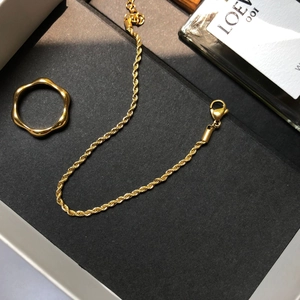 Gros plan sur la gourmette dorée torsadée et la bague ondulée dans un coffret noir