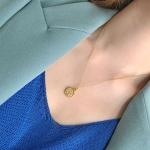 Close-up of gold coin pendant necklace worn with a layered chic outfit
