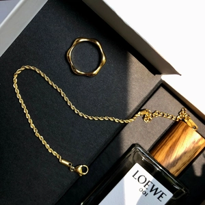 Gros plan du bracelet chaîne torsadée dorée et bague vague dans un écrin noir élégant
