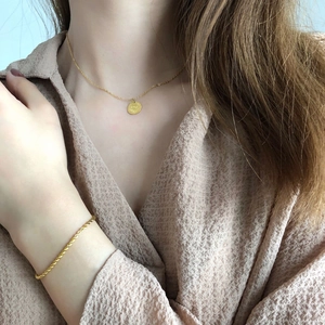 Gros plan d'un bracelet gourmette doré et d'un collier pendentif pièce sur modèle