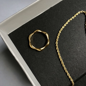 Macro detail of wave shaped gold ring and twisted rope chain on textured jewelry display