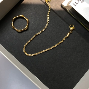 Gros plan d'une bague dorée ondulée et d'un bracelet chaîne torsadé dans un écrin cadeau
