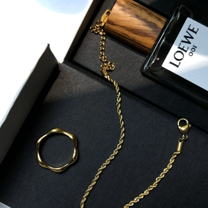 Détail d'une bague dorée ondulée et d'une chaîne torsadée dans un coffret cadeau noir chic