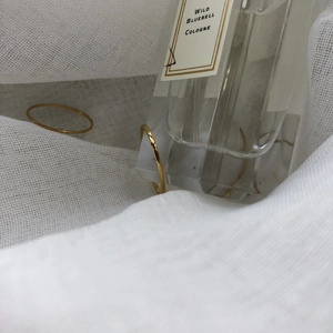 Minimalist slim gold ring set displayed on white fabric next to a perfume bottle