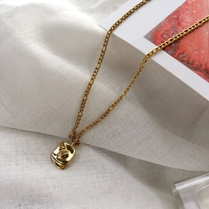 Detail of a gold abstract face square pendant necklace with unique embossed texture