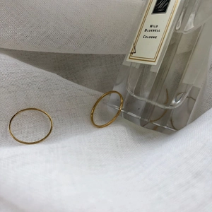Detail of two minimalist gold thin band rings placed on white textured fabric