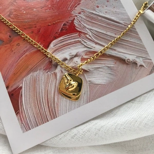 Close-up of golden necklace with abstract face embossed square pendant on art card