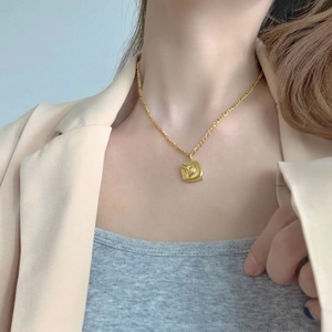 Detail of a gold rectangular pendant featuring an abstract face relief on a fine chain