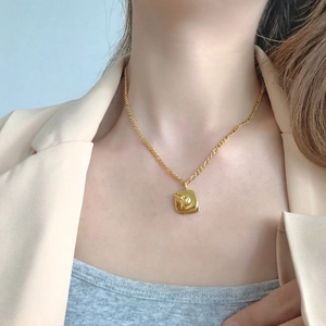 Close-up of gold relief square pendant necklace on model with minimalist business attire
