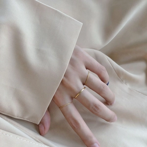 Ensemble de bagues minimalistes en titane doré 18 carats portées sur fond beige