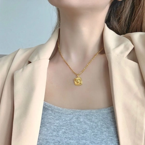 Detailed close-up of golden abstract face square pendant on a classic thin necklace