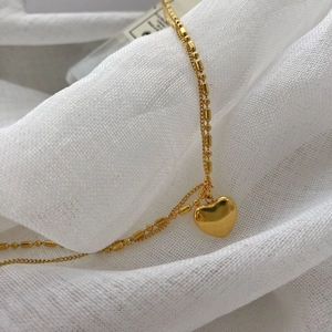 Vintage layered gold necklace with heart pendant on white textured fabric background