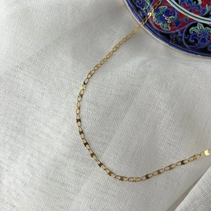 Macro detail of golden lip chain necklace showing polished oval links on white fabric