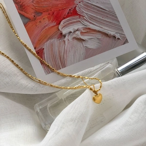 Close-up of golden double-layer chain necklace with solid heart pendant on white fabric