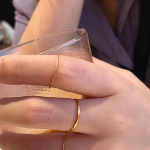 Vue rapprochée de bagues dorées minimalistes empilées sur une main tenant un verre