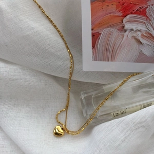 Detailed macro of a vintage golden heart pendant necklace on a clean white textured fabric