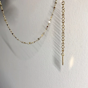 Detail of gold geometric choker showing interconnected round links and a long metal bar pendant
