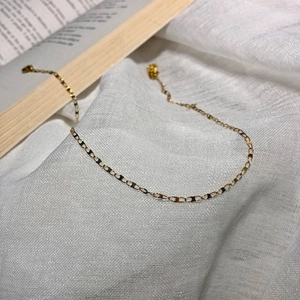 Macro detail of minimalist gold oval link necklace on a rustic white textured background