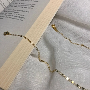 Detail of a thin gold choker necklace with flat cross chain links and lobster clasp