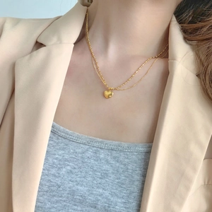 Close-up of a double-layered gold heart pendant necklace worn with a beige blazer