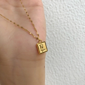 Gros plan du collier pendentif carré doré avec un relief délicat de fleur de rose chic