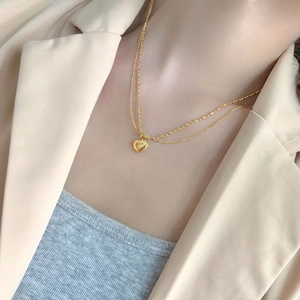 Detail of a layered gold heart pendant necklace on a model wearing a beige blazer