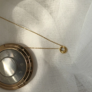 Detailed close-up of a gold hollow circle pendant on a fine chain over white fabric