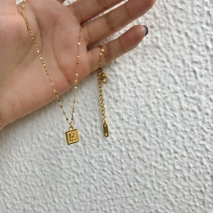 Collier minimaliste en acier titane doré avec pendentif rose tenu à la main