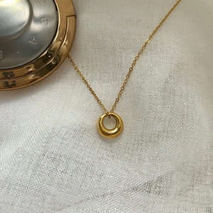 Detailed view of a minimalist gold ring necklace on white textured fabric background
