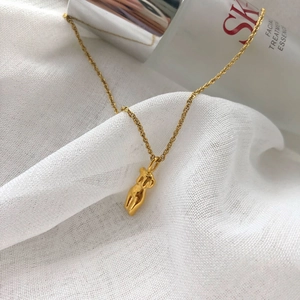 Collier avec pendentif torse féminin doré sur fond de tissu blanc texturé