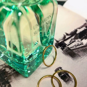 Macro shot of three polished 18K gold minimalist thin band rings on a glass perfume bottle