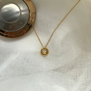 Minimalist gold circle pendant necklace on a soft white fabric background